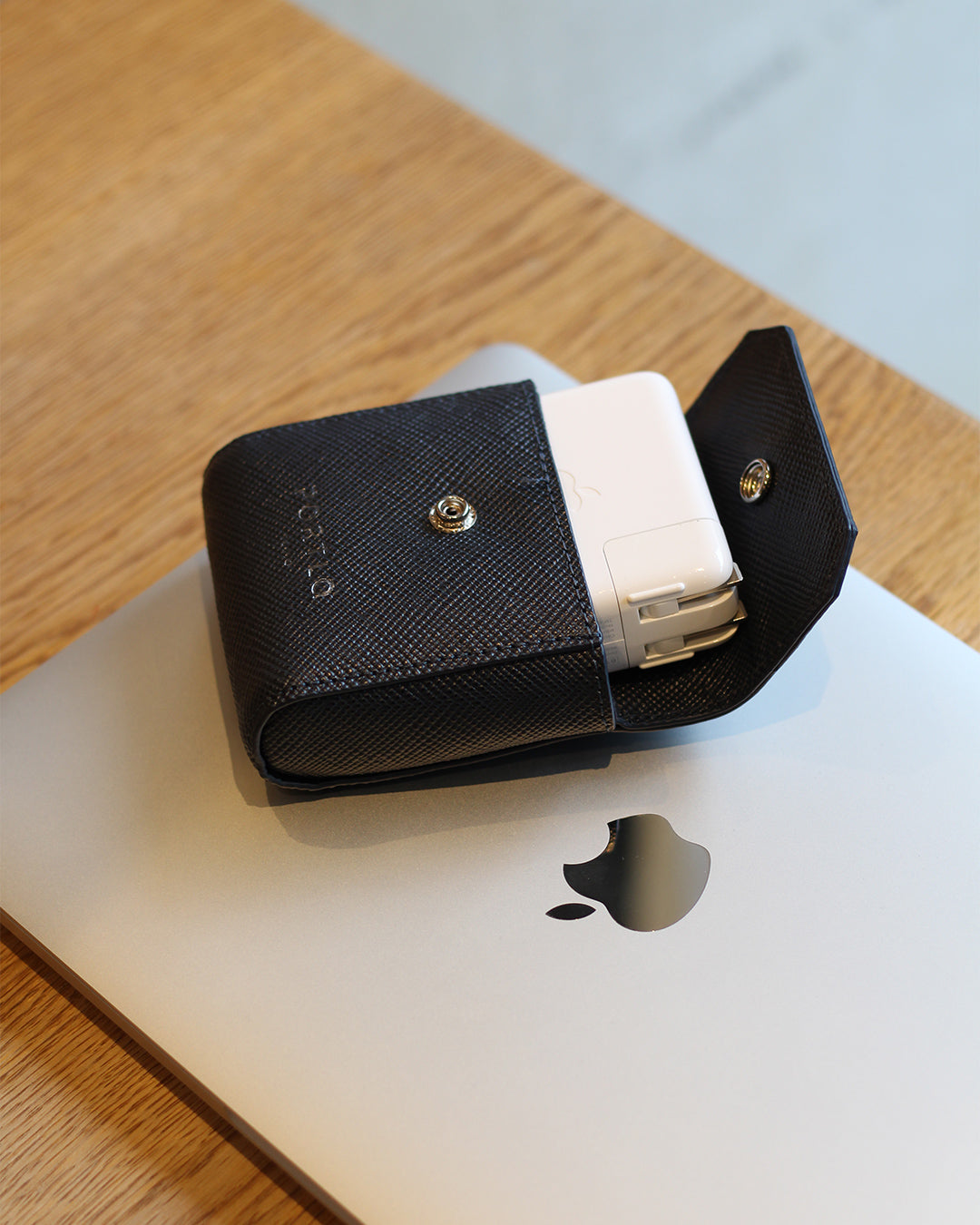 MacBookの上に置いた、PORTLAのMac電源ポーチ(ブラック)。中に電源アダプターが入っている