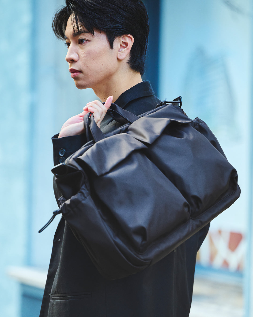 黒いジャケットの男性が、PORTLAの3WAYダッフルバッグ(ブラック)を抱えている