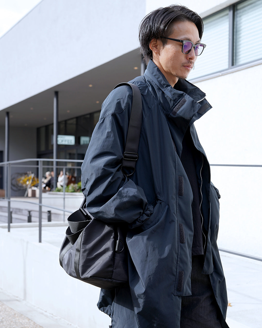 ネイビーのコートを着た眼鏡の男性が、PORTLAの2wayボストンバッグを斜め掛けにしている