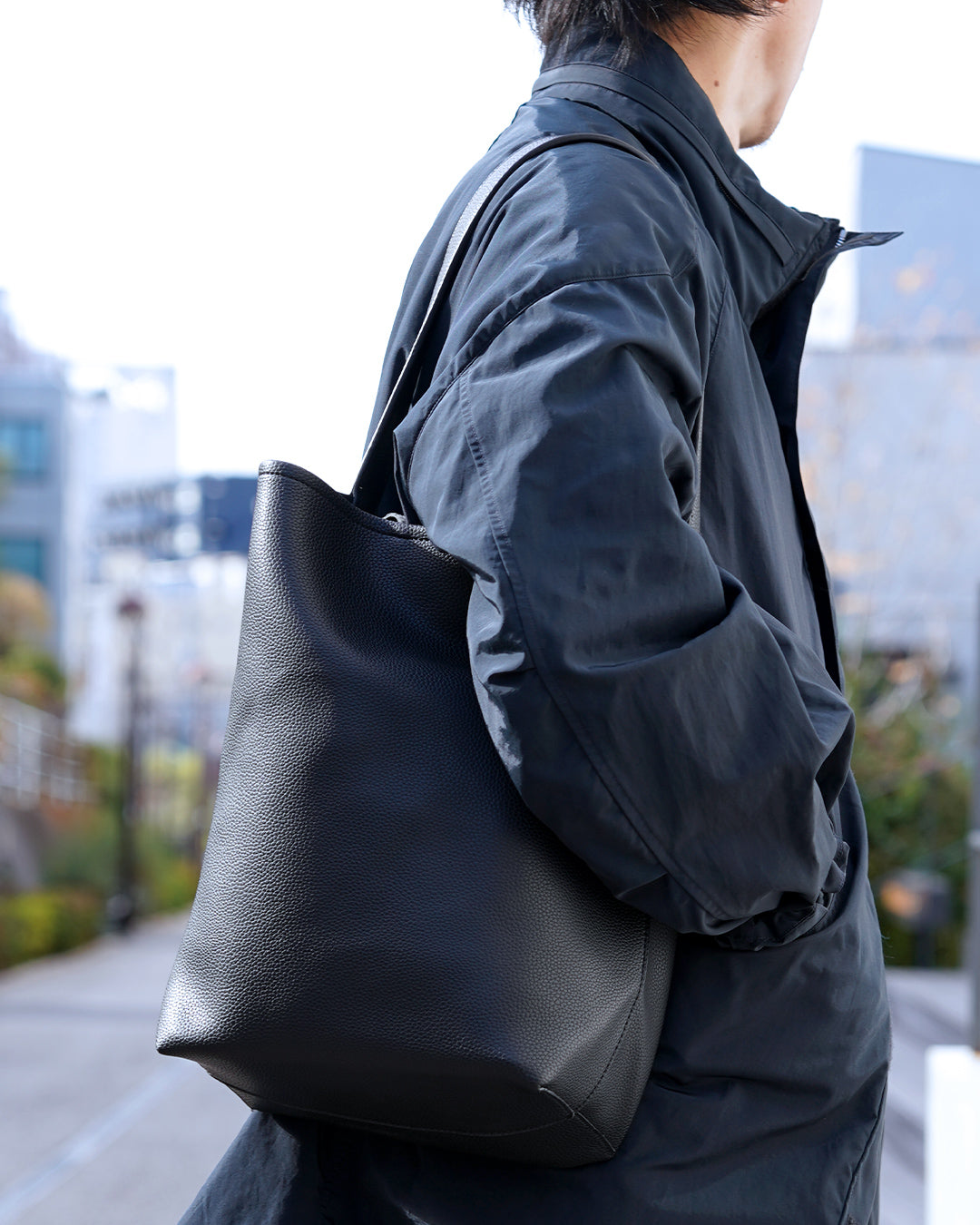 ネイビーのコートの男性が、PORTLAのバケツトートバッグ（ブラック）を肩に掛けている